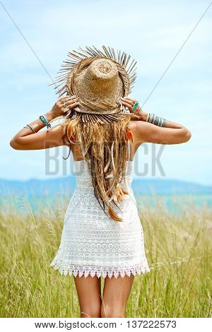 Attractive boho style woman in straw hat. Back view