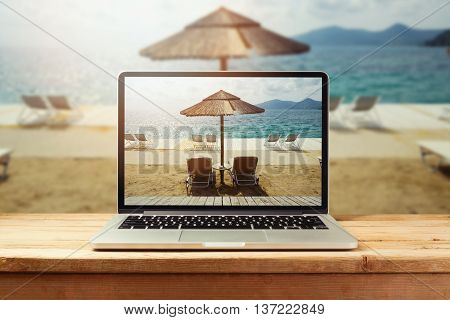 Laptop computer with sunny beach image on wooden table. Summer vacation photo sharing