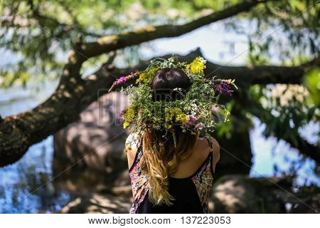 beautiful girl in a wreath of flowers on the banks of the river on a Sunny day. The pagan rite of a young girl of Midsummer. Earth Day