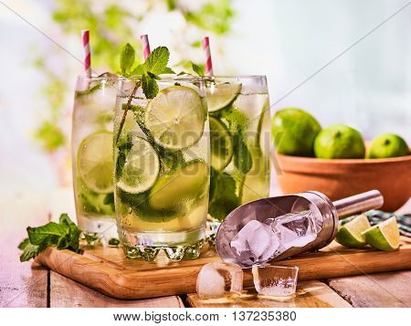 Alcohol drink. On wooden boards three glasses with alcohol drink and ice cubes. A drink number thirty six cocktail mohito and scoop ice with straw. Country life. Outdoor. Light background.