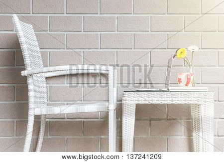 Closeup artificial colorful flower on glass bottle and computer on wood weave table with wood weave chair on blurred brown brick wall texture background beautiful interior in relaxation concept