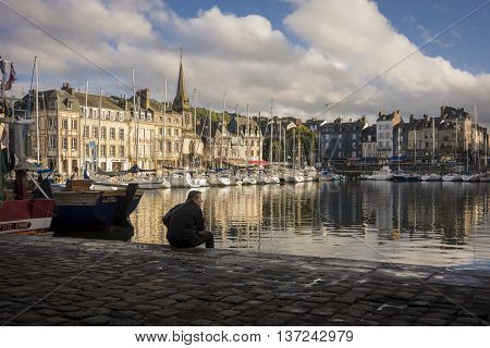 HONFLEUR HARBOUR, HONFLEUR, NORMANDY, FRANCE, 9 SEPTEMBER 2013 - Solitary man sitting on the quayside looking out over Honfleur harbour France lit by the evening sunshine France