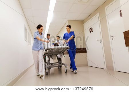 profession, people, health care, reanimation and medicine concept - group of medics or doctors carrying unconscious woman patient on hospital gurney to emergency