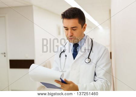 medicine, healthcare and people concept - doctor writing to clipboard at hospital