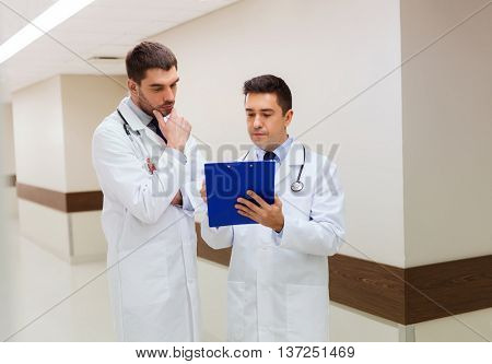 medicine, healthcare and people concept - two male doctors with clipboard at hospital corridor
