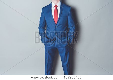 Portrait of successful businessman wearing blue siut and red tie against gray background