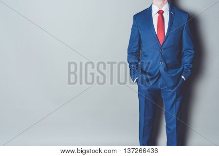 Portrait of successful businessman wearing blue siut and red tie against gray background