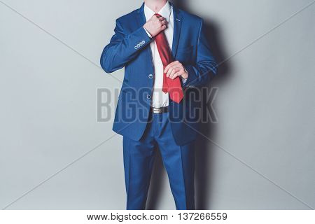 Portrait of successful businessman wearing blue siut and red tie against gray background