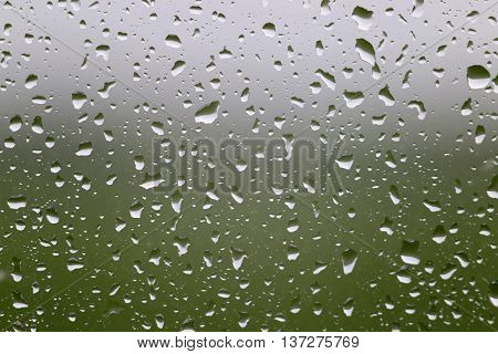 Rainy weather. Water raindrop on window glass with green meadow and gray sky