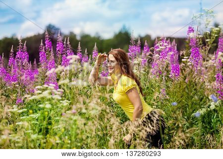 Beautiful young girl in a field of purple flowers looking into the distance put his hands to his eyes