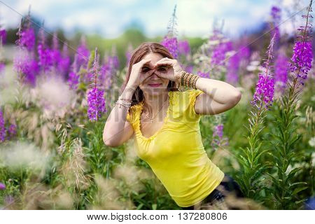 Beautiful young girl in a field of purple flowers looking into the distance put his hands to his eyes