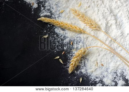 Whole flour and wheat ears on black background