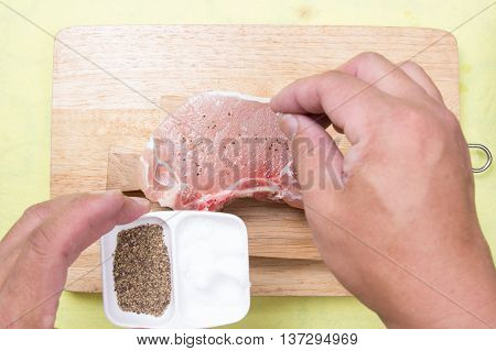 Chef putting salt to raw porkchop / cooking porkchop steak concept