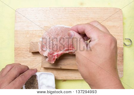 Chef putting pepper to raw porkchop / cooking porkchop steak concept