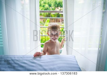 A boy stands in the room in front of the bed and smiling happy
