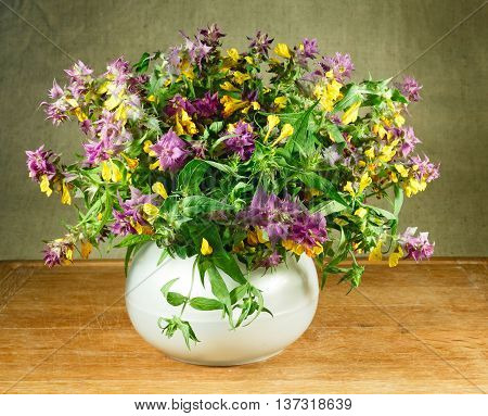 Melampyrum nemorosum. Still life. Bouquet of meadow flowers in white pots standing on a wooden table. Rustic style.