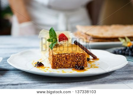 Plate with piece of cake. Cinammon stick on fresh cake. Honey cake on restaurant table. Pastry made of natural ingredients.