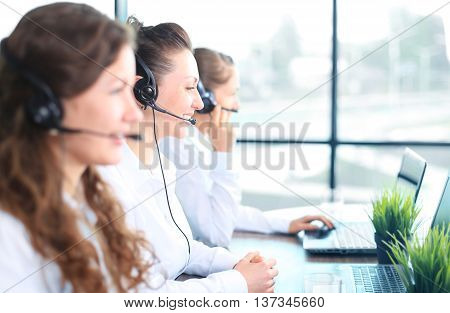 Portrait of smiling female customer service agent wearing headset with colleagues working in background at office