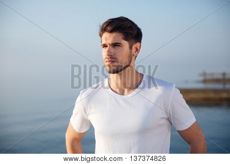 Portrait of attractive young man in white t-shirt standing near the sea