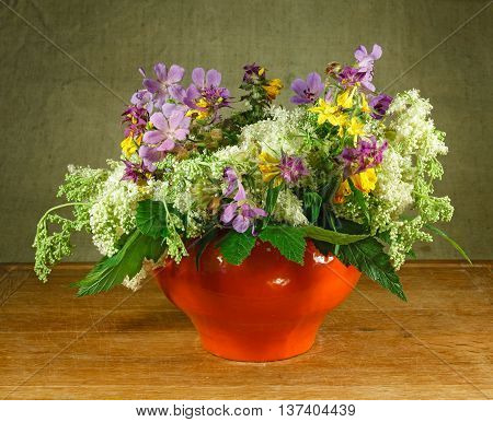 Still life. Bouquet of meadow flowers in orange pots standing on a wooden table. Rustic style. Meadow geranium meadowsweet hypericum perforatum melampyrum nemorosum .