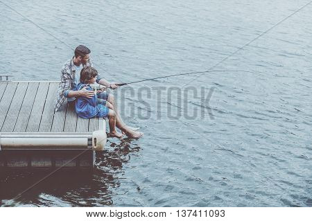 Fishing together. Top view of father and son fishing together while sitting on quayside