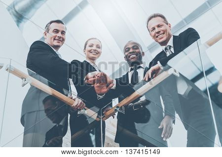Strong and successful business team. Low angle view of four confident business people standing close to each other and holding hands together