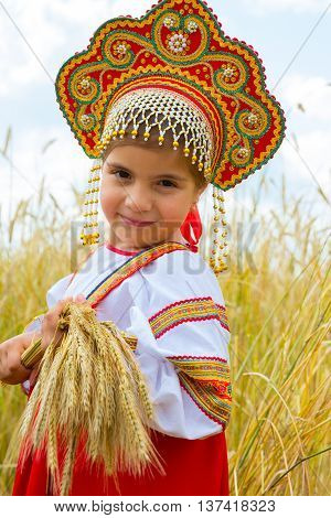 Littl girl in Russian national sarafan and a kokoshnik standing in a wheat field in summer day