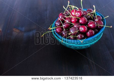red cherries in green ceramic bowl on dark background