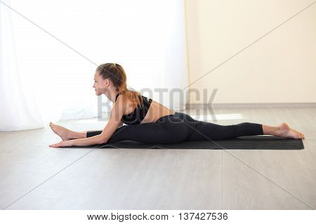 Young Woman Stretching Legs in Splits Position on yoga mat in bright room. Working on Flexbility and stretch the muscles.