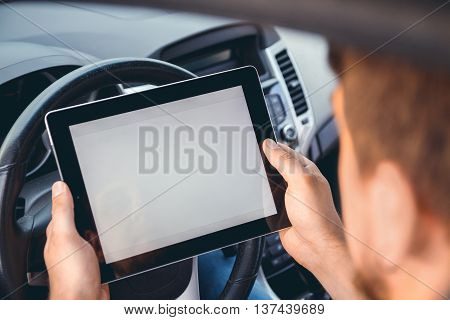 A young man with a tablet in his hand at the wheel of the car. Multitasking. Safe driving concep
