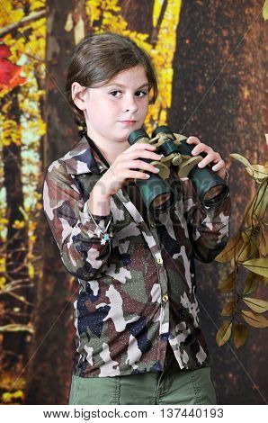 An adorable elementary brunette looking up from her binoculars as she's exploring the autumn woods.