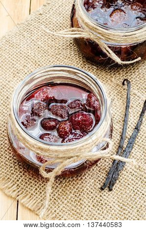 Strawberry jam in a glass jar on sackcloth with vanilla pods on wooden table