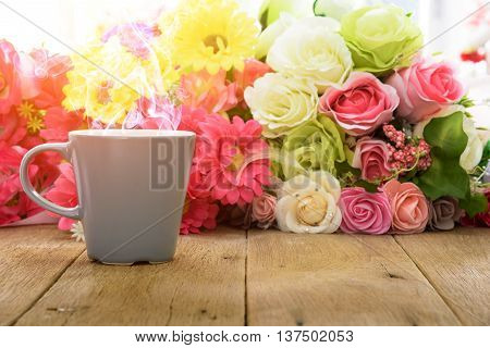 Cup of hot coffee on a wooden table with flower background under morning sunlight