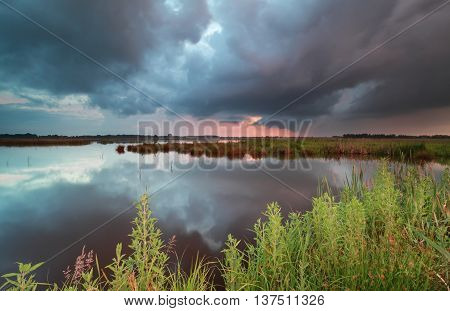 stormy sunset sky over wild lake in summer