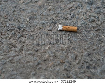 One orange used cigarette on a pavement.