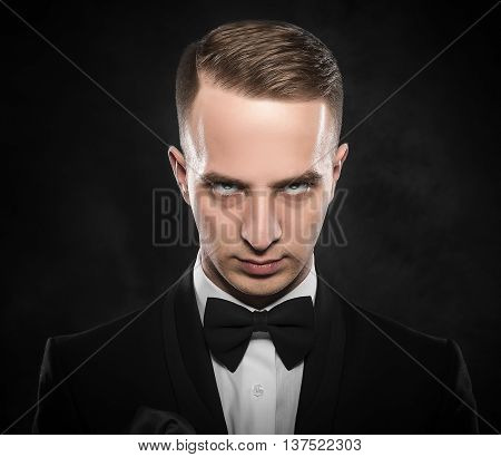 Elegant young man in suit looking frowning on dark background.