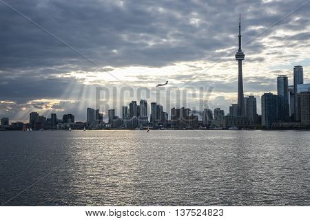 THE TORONTO CITY SKYLINE WITH SUNBEAMS AND AN AIRPLANE IN THE DISTANCE