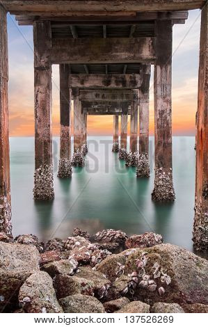 Underneath the pylons of a long jetty pier beach overlooking the sea at sunset or twilight at Khao Laem Ya Mu Ko Samet National Park Rayong Thailand. Seascape long exposure shot