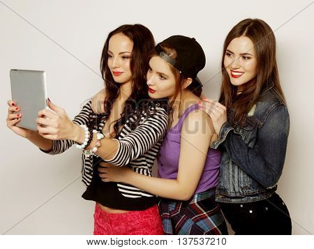 Three girls friends taking selfie with digital tablet, studio shot over gray vackground