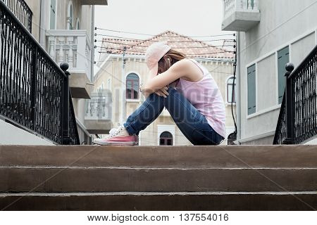 sad woman wearing a hat and hugging knees on stairdark tone.