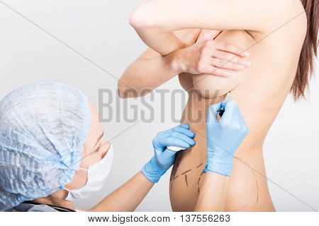 Female doctor makes dotted line on female body for cellulite correction. cosmetic surgery. lifting and breast augmentation.