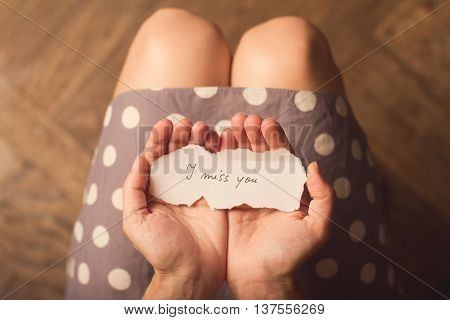 Top view of woman in dotted dress holding a paper message with the text I miss you