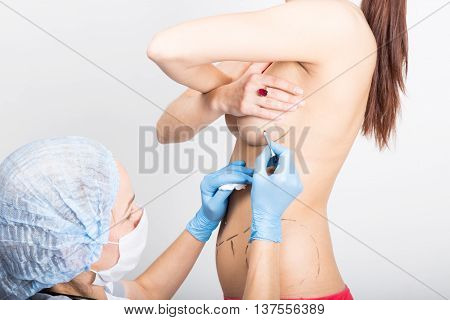 Female doctor makes dotted line on female body for cellulite correction. cosmetic surgery. lifting and breast augmentation.