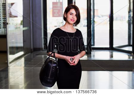 Office worker beautiful young businesswoman in black dress walking with briefcase in contemporary building. looking and smiling