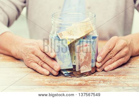 savings, money, annuity insurance, retirement and people concept - close up of senior woman hands with money in glass jar