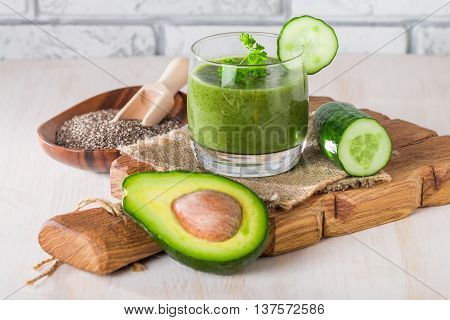 Healthy green juice smoothie surrounded by avocado, cucumber,  celery and chia seeds on white background