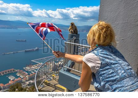 Tourist woman holding an English flag observes one of the famous monkeys of Gibraltar from the top of Gibraltar Rock, in the Upper Rock Natural Reserve.