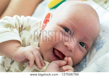 The baby is lying and smiling looking with interest.