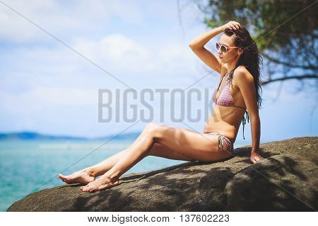 Young girl sitting on a rock holding their hair tans in sun glasses