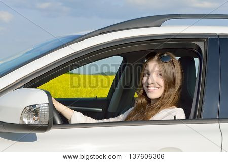 Teen Drivers - Happy teenage female driver sitting in her car which is standing in front of a canola field